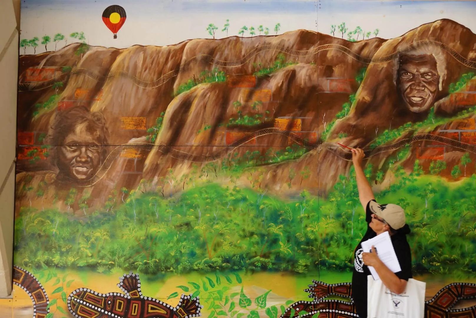 A guide pointing to details in a large painted mural.