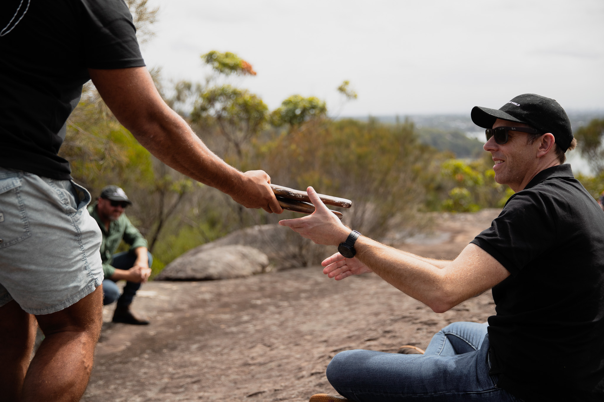 A guest receiving clapsticks during an outdoor cultural experience.